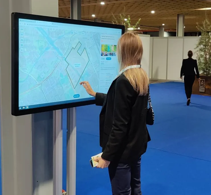 Op een beurs verkent iemand een projectgebied op de kaart, op een touchscreen